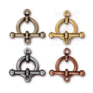 May include: Four toggle clasps in different finishes: antique brass, gold, silver, and copper. Each clasp features a round ring and a bar with two ball-shaped ends.