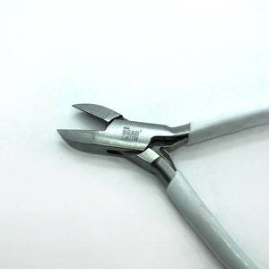 May include: A pair of BergSmith flush cutters with silver metal blades and white handles. The text "the Berg Smith" is printed on the tool. This tool is designed for precision cutting and is suitable for various craft projects.