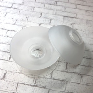 Peut inclure: Deux abat-jours en verre dépoli, un rond et un ovale, sont présentés sur un fond de briques blanches. Les abat-jours ont un anneau en plastique transparent autour de l'ouverture. L'abat-jour rond est plus grand que l'abat-jour ovale.