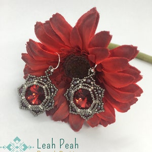 May include: A pair of silver and red beaded earrings with a red crystal centerpiece. The earrings are displayed on a red flower.
