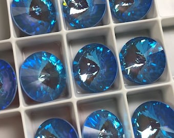 May include: A collection of 10 round, faceted, light blue glass rhinestones in a white plastic tray. The rhinestones are arranged in rows and columns.