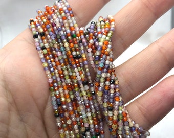 May include: A strand of tiny, faceted, multi-colored gemstone beads in shades of orange, purple, yellow, green, and clear. The small, round, reflective beads are strung together in a dense, textured cluster, showcasing a variety of vibrant hues.