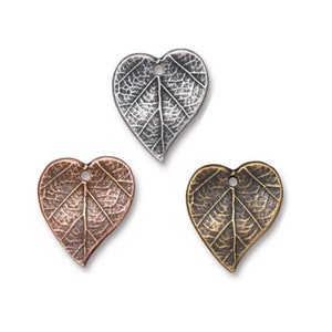 Op de afbeelding: Drie hartvormige metalen bedels met een bladontwerp. De bedels zijn in zilver, koper en antiek messing.