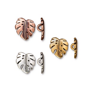 May include: Set of three pairs of decorative buttons featuring a heart-shaped monstera leaf design. The buttons are available in copper, gold, and silver finishes.