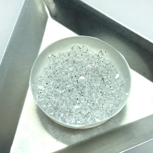 May include: A white bowl filled with clear glass beads. The beads are small and have a faceted shape.