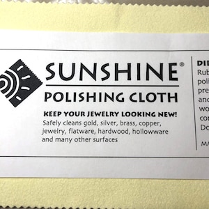 May include: A white rectangular Sunshine Polishing Cloth product label with black text and a logo. The label reads "Keep Your Jewelry Looking New!" and lists materials the cloth cleans, including gold and silver.