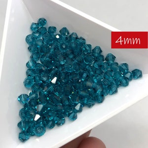 May include: A close-up of a pile of teal blue 4mm glass beads. The beads are faceted and have a shiny finish.