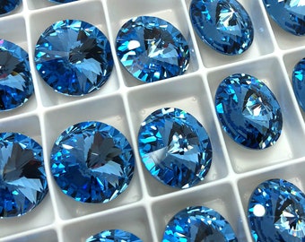 May include: A close-up view of a tray of round, blue, faceted glass rhinestones. The rhinestones are arranged in a grid pattern and are all the same size.