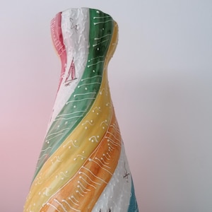 May include: A decorative vase with a colourful, striped design. The vase has a spiral pattern of red, white, green, yellow, orange, and blue. Small sailboat illustrations are painted on the white stripes. A unique piece of home decor, approximately 30 cm tall.