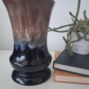 May include: A decorative ceramic vase with a flared rim and a rounded base. The vase has a colour gradient, starting with dark brown at the top, fading to blue and then black at the base. A small cactus in a white pot is next to the vase.