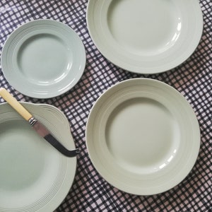May include: Four pale green ceramic plates with a ridged design. The plates are arranged on a black and white checked tablecloth.