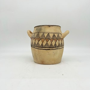 May include: A small, cream-colored ceramic pot with two handles. The pot has a geometric pattern of brown and orange triangles.