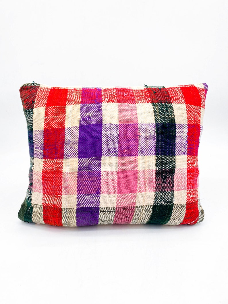 May include: A rectangular pillow with a plaid pattern in red, pink, purple, and green. The pillow is made of a woven fabric and has a slightly distressed look.