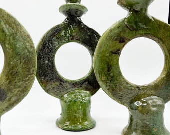 Op de afbeelding: Drie handgemaakte groene keramische kandelaars. Elk heeft een cirkelvormig ontwerp met een centrale opening, een voetstuk en een bovenkant die is ontworpen om een kaars vast te houden. De keramische stukken hebben een getextureerde, geglazuurde afwerking.