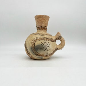 May include: A small, brown ceramic vase with a narrow neck and a single handle. The vase is decorated with a geometric pattern in brown paint.