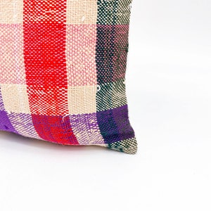 May include: A colorful woven pillow with a plaid pattern in shades of red, pink, purple, green, and white.