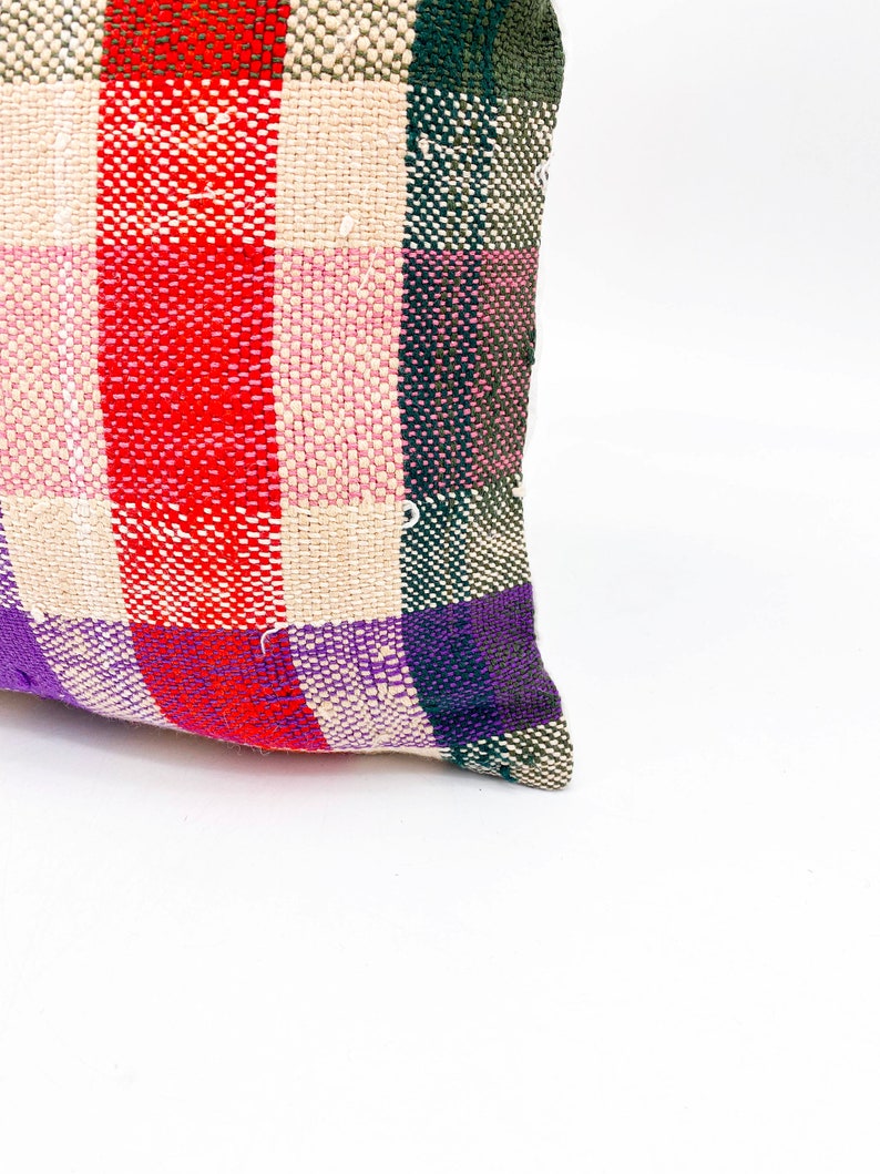 May include: A colorful woven pillow with a plaid pattern in shades of red, pink, purple, green, and white.