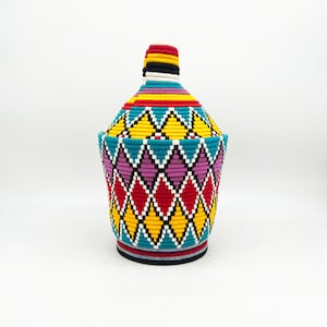 May include: A colorful woven basket with a diamond pattern in shades of red, yellow, blue, and pink. The basket has a lid and is made of a natural fiber.