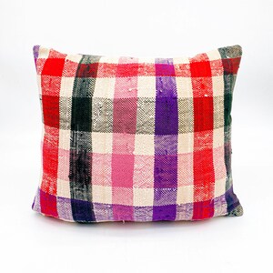 May include: A rectangular pillow with a plaid pattern in shades of red, pink, purple, black, and white.