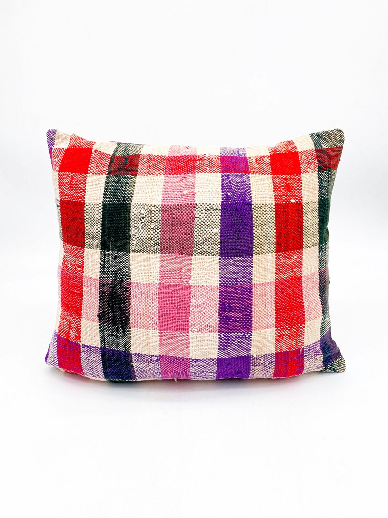 May include: A rectangular pillow with a plaid pattern in shades of red, pink, purple, black, and white.