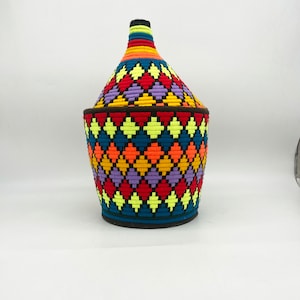 May include: A colorful woven basket with a diamond pattern in shades of red, orange, yellow, blue, purple, and green. The basket has a rounded top and a wide base.