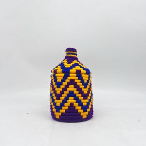 May include: A woven basket with a lid, featuring a chevron pattern in purple, yellow, and blue. The basket has a cylindrical body and a rounded top, suitable for storage or decoration.