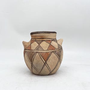 May include: A small, rounded ceramic vessel with a wide opening and two small side handles. The exterior features a light tan base color decorated with a repeating geometric pattern of dark brown intersecting lines and filled-in reddish-brown triangles.