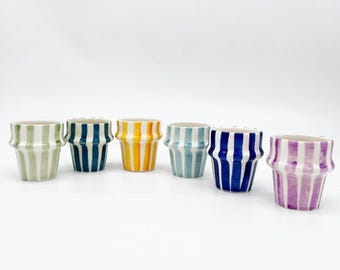 May include: Six small ceramic pots in a row, each with a unique color scheme. The pots feature vertical stripes in green and white, navy and white, yellow and white, light blue and white, dark blue and white, and purple and white. The pots have a flared shape.
