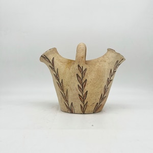 May include: A beige ceramic vase with a brown leaf design. The vase has three openings and a handle.
