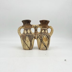 May include: A pair of brown ceramic vases with geometric designs, connected at the base. The vases have a light brown color and are decorated with dark brown lines and shapes.
