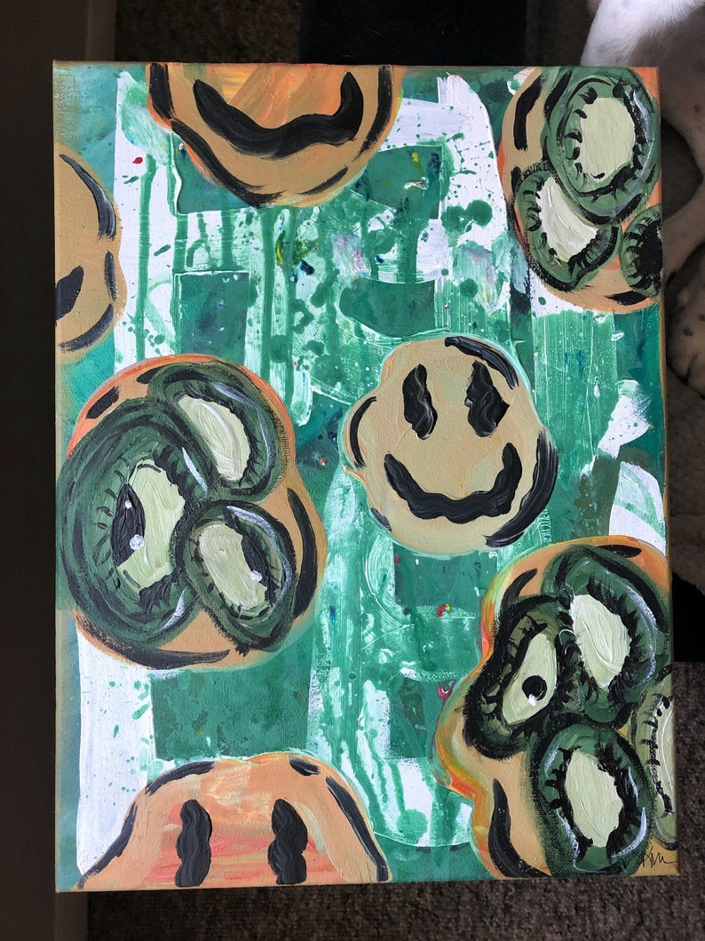 May include: Abstract painting on canvas with a green background and multiple smiley faces in different colours and styles. Some of the smiley faces have eyes and others have a more simple design.
