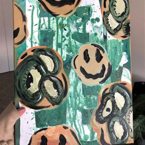 May include: Abstract painting on canvas with a green background and multiple smiley faces in various shades of green, yellow, and orange. The smiley faces are painted in a simple style with black outlines.