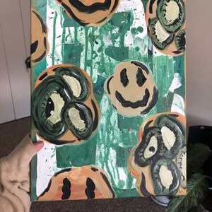 May include: Abstract painting on canvas with a green background and multiple smiley faces in various shades of green, yellow, and brown.