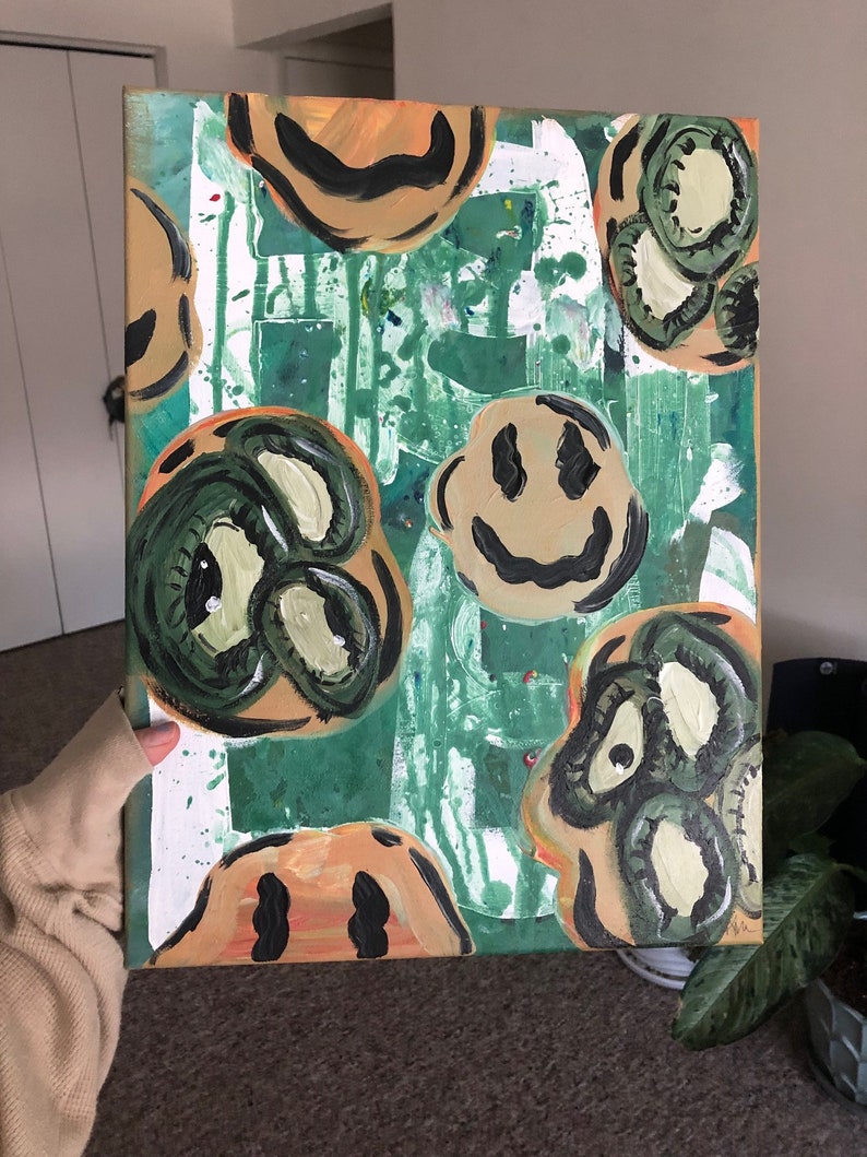 May include: Abstract painting on canvas with a green background and multiple smiley faces in various shades of green, yellow, and brown.