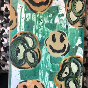 May include: Abstract painting on canvas with a green, white and orange background. The painting features multiple smiley faces with black outlines and green and yellow eyes.