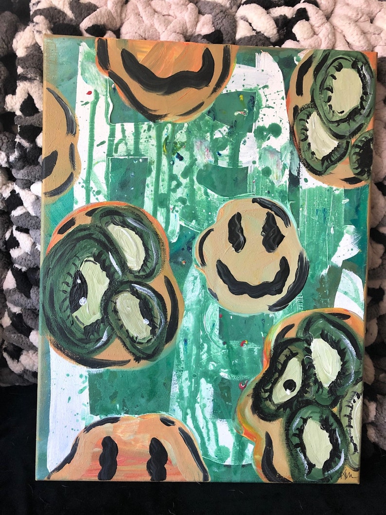 May include: Abstract painting on canvas with a green, white and orange background. The painting features multiple smiley faces with black outlines and green and yellow eyes.