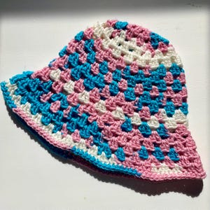 May include: A crocheted bucket hat with a pink, white and blue colour pattern.