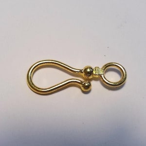 May include: A gold-toned metal hook clasp featuring a smooth, curved design with a rounded ball tip at the end of the hook. The clasp includes a small, circular ring attached to a central ball-shaped connector, providing a secure closure mechanism.