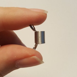 May include: A silver metal spring clasp with a coil design. The clasp is held between two fingers.