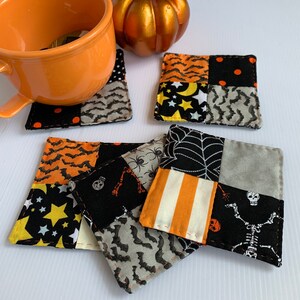 May include: A set of Halloween-themed fabric coasters. Each coaster is a patchwork of various Halloween patterns, including bats, stars, and stripes. An orange mug and a decorative pumpkin are also in the image.