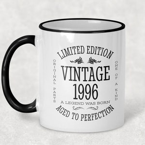 May include: White ceramic coffee mug with a black handle and black rim. The mug has black text that reads "Limited Edition Original Parts Vintage 1996 A Legend Was Born Aged to Perfection One of a Kind".