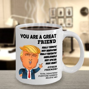 May include: White ceramic coffee mug with a cartoon image of Donald Trump. The mug has black text that reads "You are a great friend. Really terrific, very handsome, really fantastic, unbelievable, very special, huge heart. Other friends? Total disasters! Everyone agrees! Believe me!"