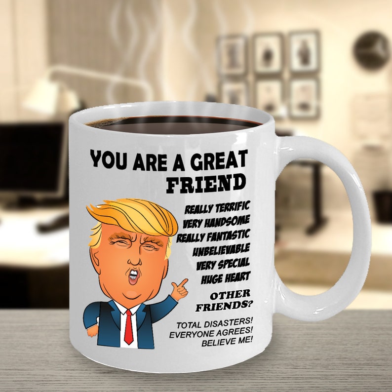 May include: White ceramic coffee mug with a cartoon image of Donald Trump. The mug has black text that reads "You are a great friend. Really terrific, very handsome, really fantastic, unbelievable, very special, huge heart. Other friends? Total disasters! Everyone agrees! Believe me!"