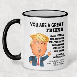 May include: White ceramic coffee mug with a black rim and handle. The mug features a cartoon image of Donald Trump with the text "You are a great friend" and a list of positive attributes, ending with "Total disasters! Everyone agrees! Believe me!"
