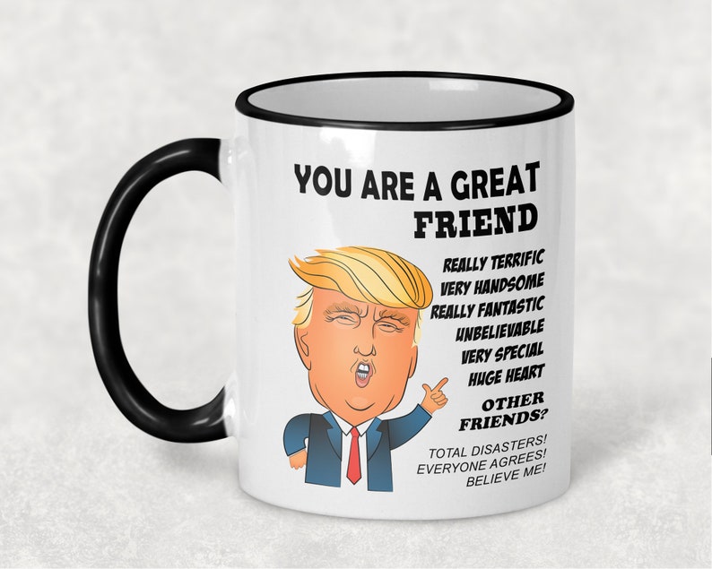 May include: White ceramic coffee mug with a black rim and handle. The mug features a cartoon image of Donald Trump with the text "You are a great friend" and a list of positive attributes, ending with "Total disasters! Everyone agrees! Believe me!"