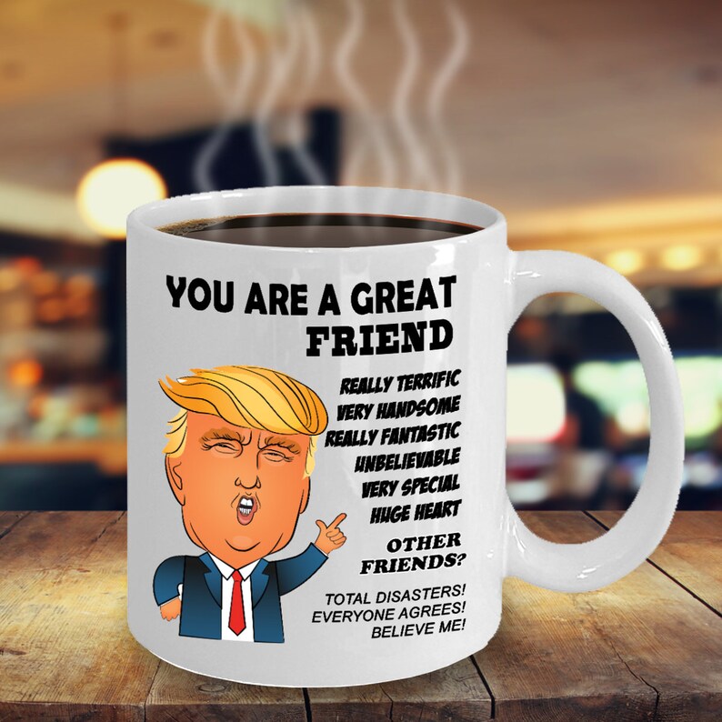 May include: White ceramic coffee mug with a cartoon image of Donald Trump. The mug has black text that reads "You are a great friend. Really terrific, very handsome, really fantastic, unbelievable, very special, huge heart. Other friends? Total disasters! Everyone agrees! Believe me!"