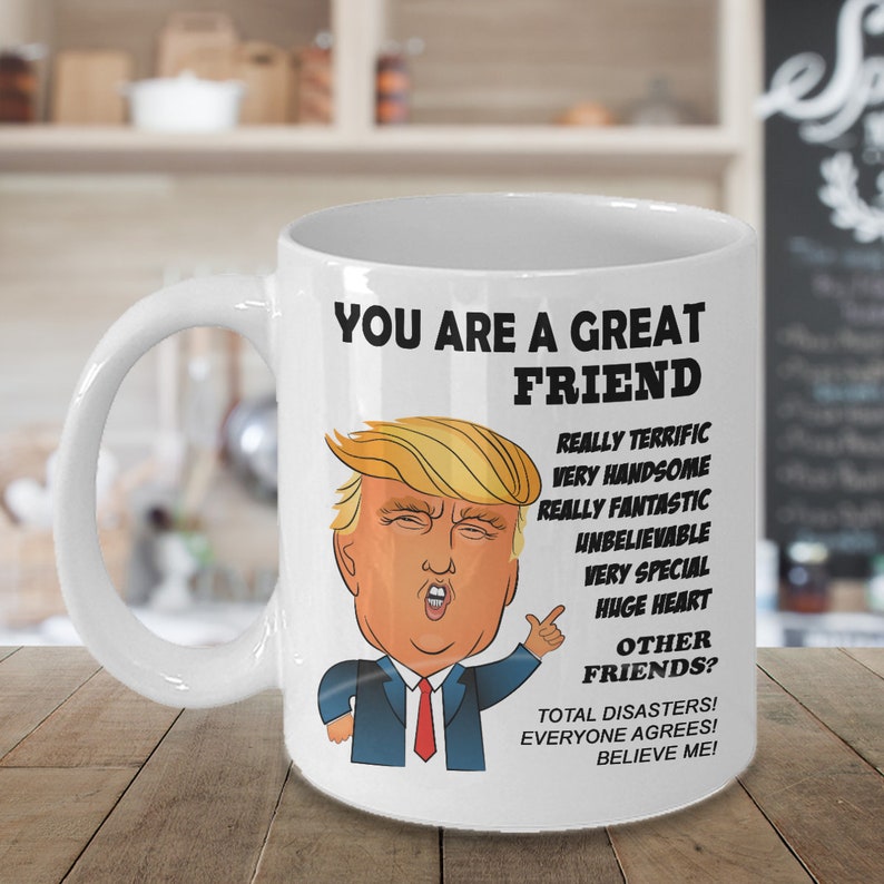 May include: White ceramic coffee mug with a cartoon image of Donald Trump. The mug reads "You are a great friend. Really terrific, very handsome, really fantastic, unbelievable, very special, huge heart. Other friends? Total disasters! Everyone agrees! Believe me!"