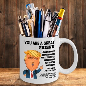 May include: White ceramic mug with a cartoon image of Donald Trump and the text "You are a great friend. Really terrific, very handsome, really fantastic, unbelievable, very special, huge heart. Other friends? Total disasters! Everyone agrees! Believe me!"