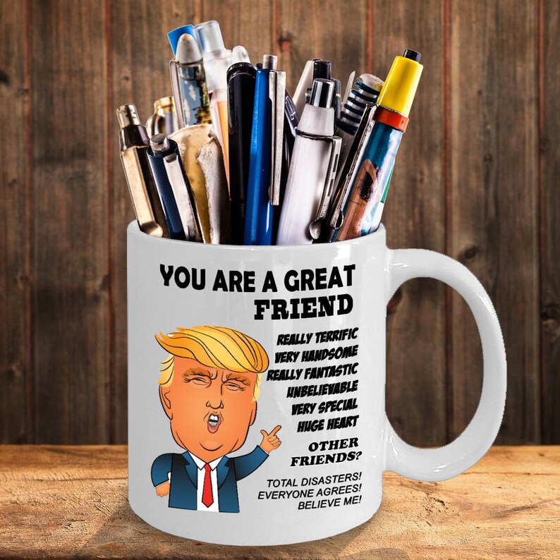 May include: White ceramic mug with a cartoon image of Donald Trump and the text "You are a great friend. Really terrific, very handsome, really fantastic, unbelievable, very special, huge heart. Other friends? Total disasters! Everyone agrees! Believe me!"