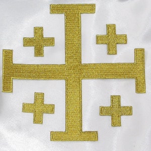 Puede incluir: Una cruz bordada en oro con cuatro cruces más pequeñas en cada esquina sobre un fondo blanco.